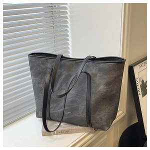 Detail of dark gray leather tote bag with industrial texture and minimal shoulder straps