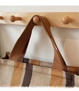 Detail of striped canvas tote bag showing wide woven handle on wooden hook