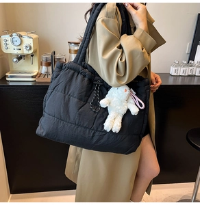 Macro shot of black quilted puffer tote bag with plush rabbit charm in cafe setting