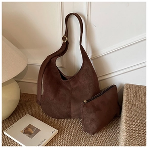 Sac hobo en daim marron foncé avec bandoulière réglable sur un tapis texturé minimaliste