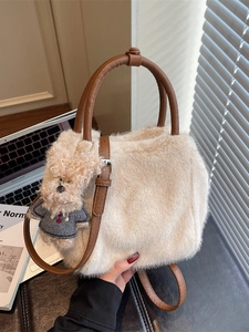 Cremefarbene Plüsch-Handtasche mit braunen Griffen und Bären-Anhänger auf Schreibtisch