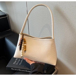 Detail of cream pleated leather baguette bag with bead charm on black books