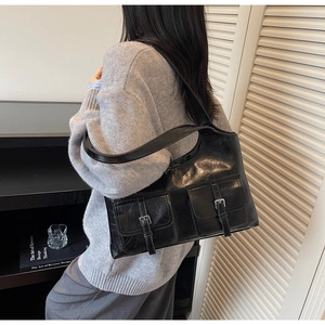 Side view of a vintage black shoulder bag with two buckle pockets and a wide strap