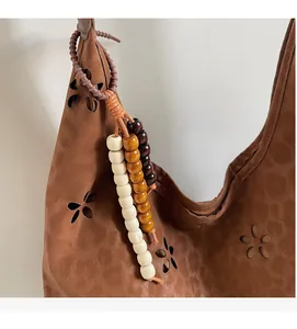 Détail du sac bandoulière en daim marron avec fleurs découpées et pompon en bois