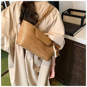 Dettaglio borsa a spalla intrecciata marrone con patta in pelle e nappa di legno