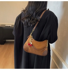 Close-up of brown suede crescent bag with gold chain and cherry charm on model shoulder