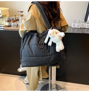 Detail of black quilted tote bag with white plush rabbit charm on a wide shoulder strap