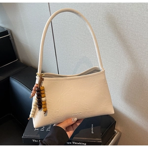 Detail of off-white faux leather handbag with colorful beaded pendant and brand logo