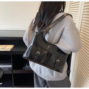 Detail of black glossy PU leather tote bag with functional front utility pockets and buckles