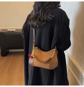 Close-up of brown suede moon bag with red cherry charm and gold chain strap detail