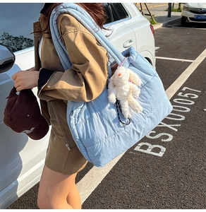 Light blue quilted puffer tote bag with a white bunny charm shown in an outdoor street style