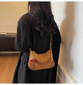 Detail van bruine suède hobo tas met gouden ketting en kersenhanger op zwarte jas