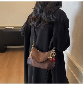 Detail van suède halve maan tas met gouden ketting en kersenhanger op model