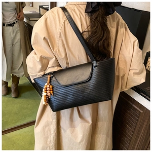 Dettaglio borsa a tracolla intrecciata nera con ciondolo di perline su un trench beige