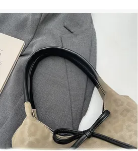 Detailed view of beige suede bucket bag with black leather handle and decorative bow