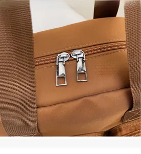 Detail of a brown tote bag featuring smooth double silver zippers and woven handles