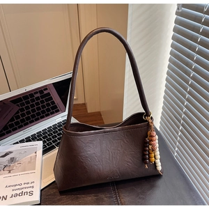 Detail of dark brown leather handbag with wooden bead charm and elegant shadow lighting