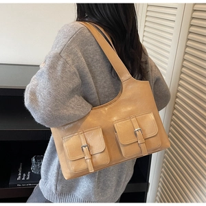 Close-up of vintage light brown shoulder bag featuring dual pockets and silver metal buckles
