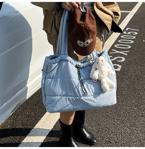 Detail of light blue quilted puffer tote bag with drawstring closure and plush bunny charm
