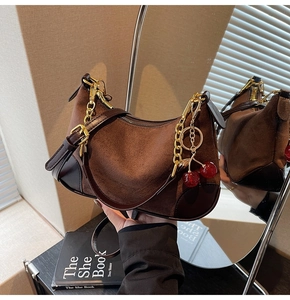 Detail of a brown suede baguette bag featuring a gold chain and red cherry charm