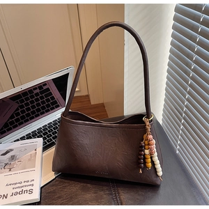 Close-up of brown faux leather shoulder bag with colorful wooden bead pendant and textures