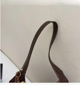Detail of dark brown leather tote with white stitching and golden ring hardware