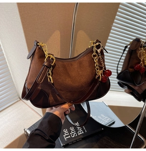 Detail of dark brown suede baguette bag with gold chain and red cherry charm