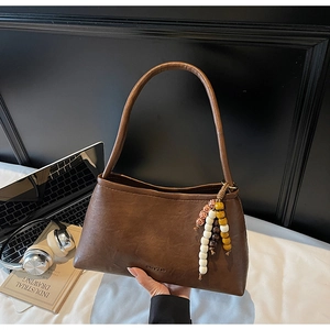 Detail of vintage brown leather underarm bag with unique wooden bead charm and brand logo