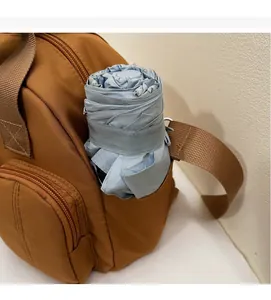 Close-up of a brown nylon shoulder bag side pocket holding a blue folding umbrella