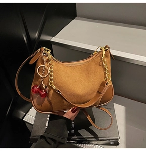 Detail of brown suede baguette bag featuring golden chain strap and cherry charm accessory