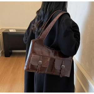 Detail of dark brown glossy leather tote bag with dual front pockets and silver buckles