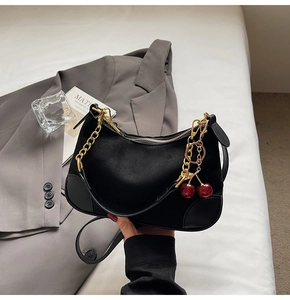 Detailed close-up of a black suede baguette bag with cherry charm and gold chain strap