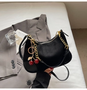 Detail of black suede hobo bag with gold chain and unique red cherry charm detail