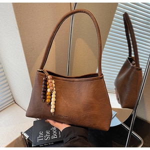 Detail view of coffee brown vintage underarm bag featuring beaded tassel and brand logo