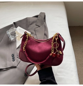 Detailed macro view of the cherry charm and gold chain on the burgundy suede baguette bag
