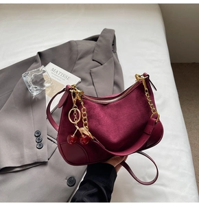 Detail of burgundy suede baguette bag with gold chain and cherry charm on blazer