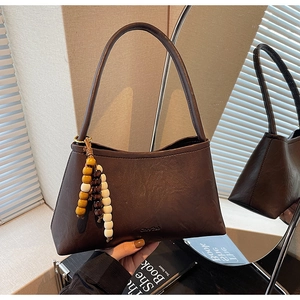 Detail of vintage dark brown faux leather underarm bag with decorative bead charm and texture