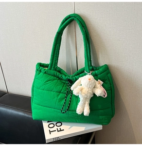 Detail of green quilted puffer tote bag with plush rabbit charm on white magazine