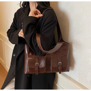 Detail of vintage brown tote bag with metal buckles on pockets against a black blazer