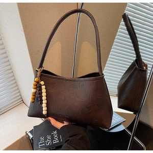 Detail of dark coffee vintage underarm bag with beaded tassel charm and PU leather texture