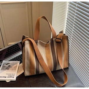 Vertical striped canvas tote bag with adjustable shoulder strap next to laptop