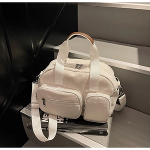 Detail of off-white canvas tote with front zip pockets and leather handles on books