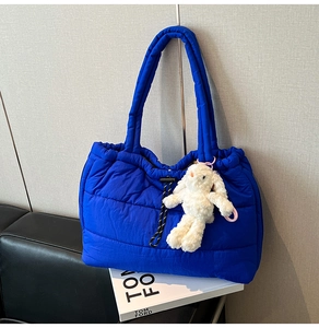 Detailed close-up of blue quilted puffer tote bag with a white plush rabbit pendant