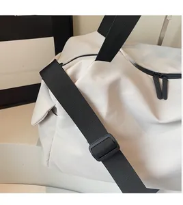 Detail of adjustable black nylon shoulder strap and smooth dual zippers on a white travel bag