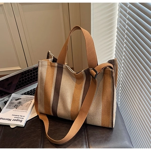 Striped canvas tote bag with adjustable shoulder strap beside a laptop in office setting