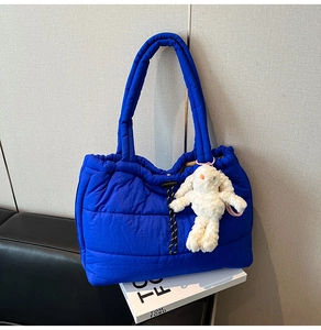 Detail of blue quilted puffer tote bag featuring drawstring closure and plush bunny charm
