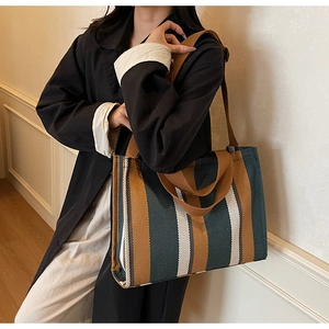 Detailed view of striped canvas tote bag with brown straps shown on a model's shoulder