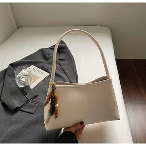 Close-up of beige baguette bag featuring wooden bead tassel and soft PU leather texture