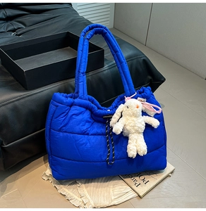 Detailed shot of bright blue quilted puffer tote bag with a white plush bunny charm
