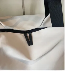 Detail view of smooth dual zippers and nylon handles on a cream sports travel bag